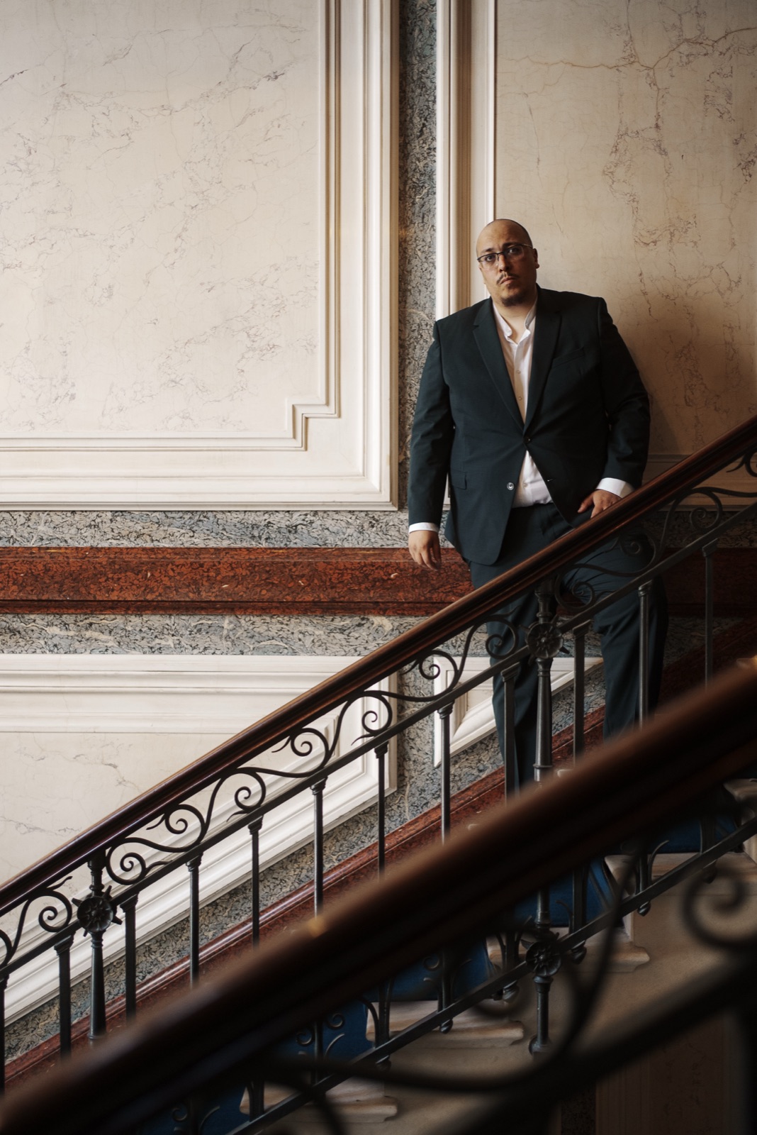 Ali Bekour, en costume, dans un escalier de marbre haussmannien